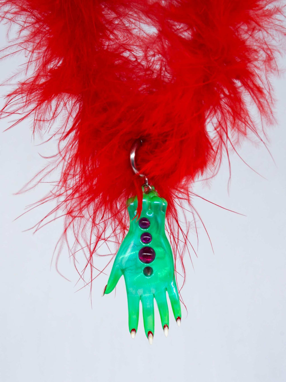 green fairy goblin hand necklace pendant with red gems on red feather background