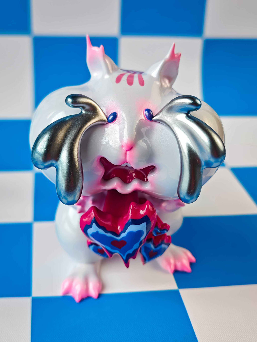 Panicky pink chipmunk figure with sparkling silver tears and vibrant heart-shaped accents, displayed on a blue and white checkered surface.