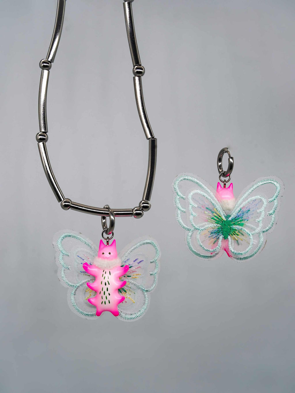 Butterfly cat with flamingo pink body and mint green wings, featuring fur snood necklace and earring.