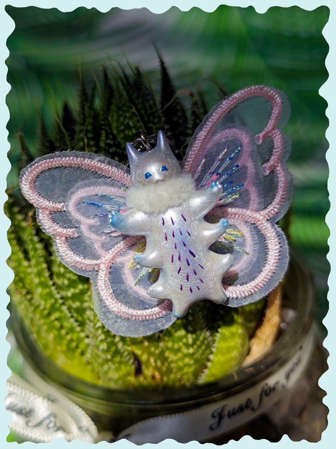 Butterfly cat with pink and white wings, embellished with purple and blue details.