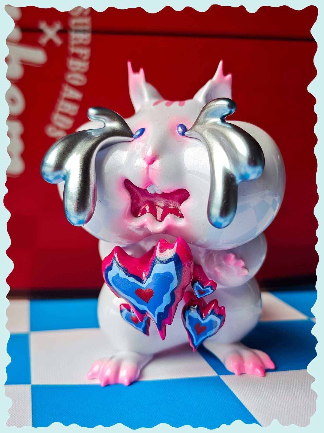 Pink chipmunk figure with metallic silver tears and heart-shaped details, set against a red background. A whimsical collectible figurine.