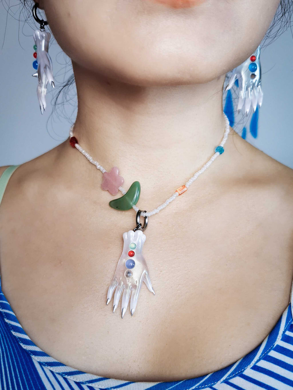 Close-up of colorful white fairy goblin monster hand earrings and necklace jewelry set on model's neck and ears
