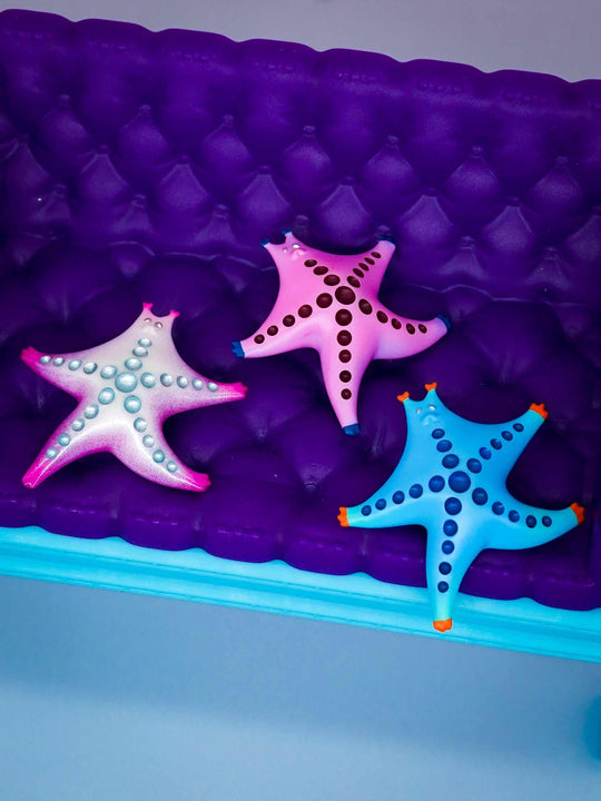 SeaStar cat hairclip and brooch in pearl color blocking and pink designs on a purple background.