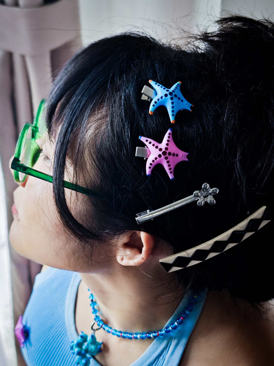 Magenta and navy SeaStar cat hairclip and brooch on dark hair.