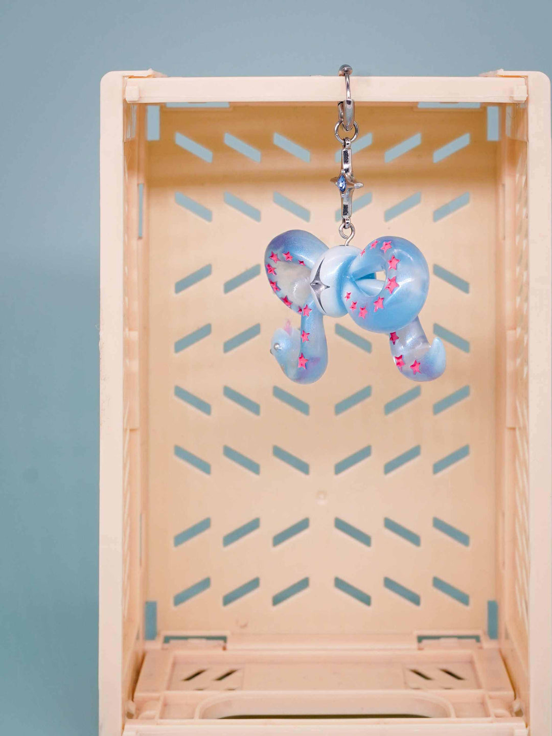 Ice blue snake bowtie keychain with pink star accents and felt tongue hanging in wooden box