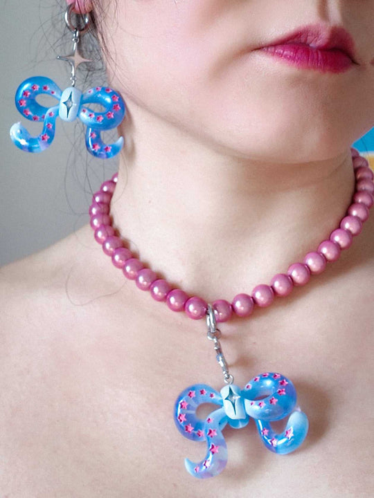 Close-up of ice blue snake bowtie necklace and earring with pink star accents on woman