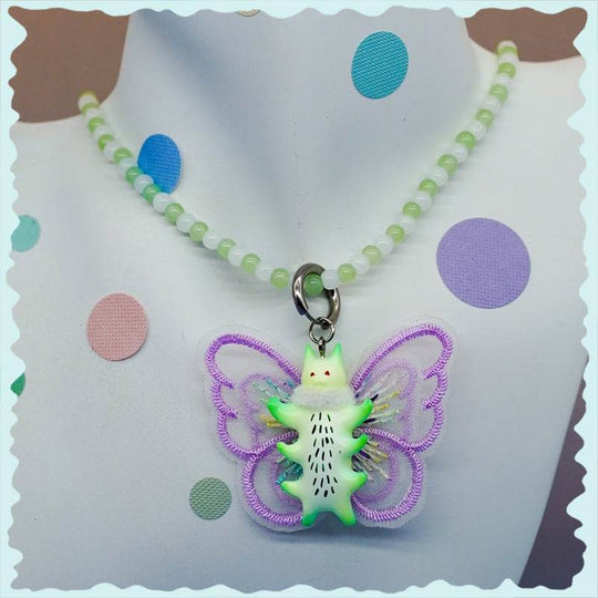 Green butterfly cat with fur snood necklace and earrings, featuring lavender wings, on a display bust.